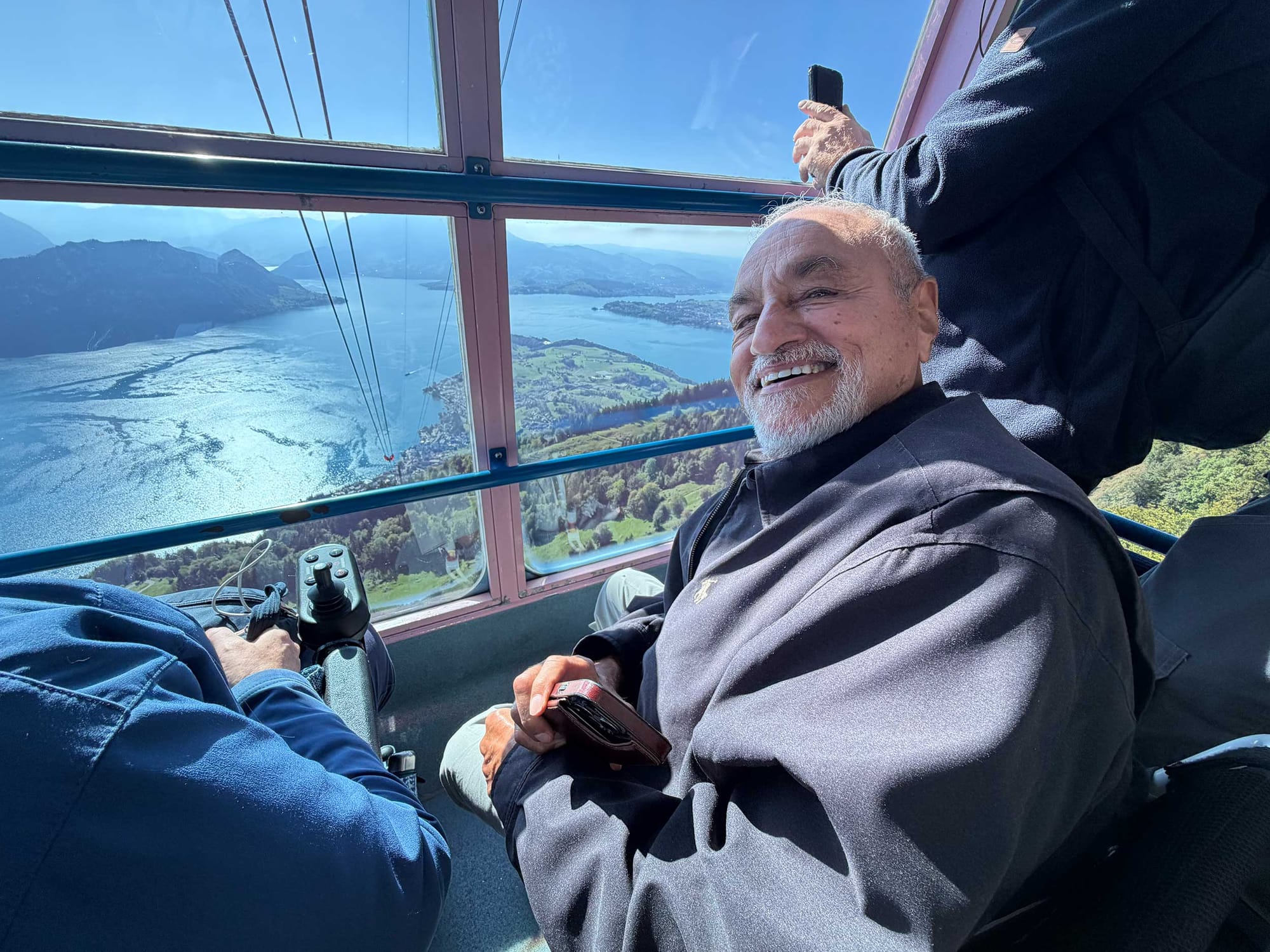 Wheelchair user smiling while a cable car descends to a Swiss lake.