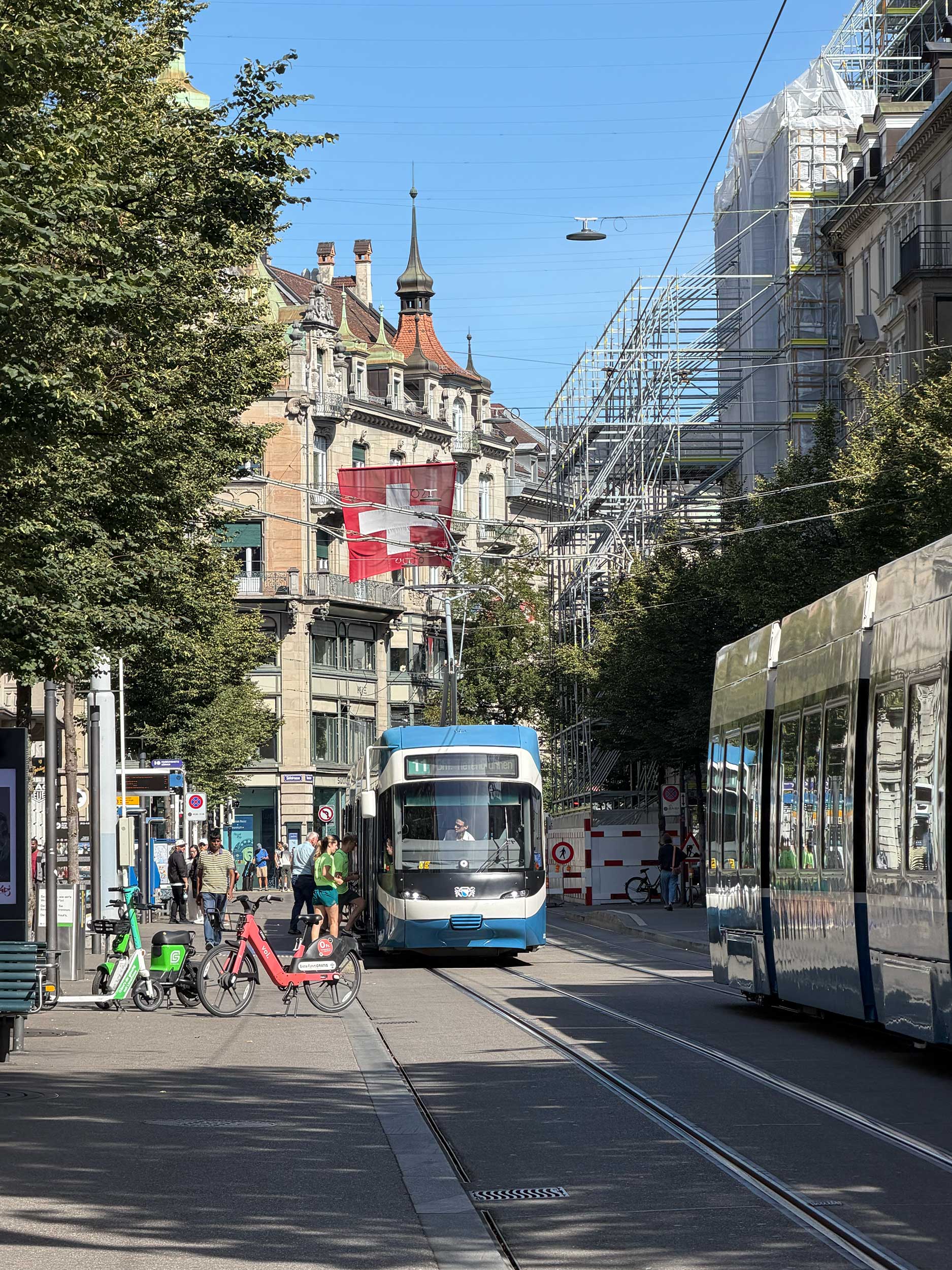 Tram on a Zurich street with a Swiss flag suspended overhead.