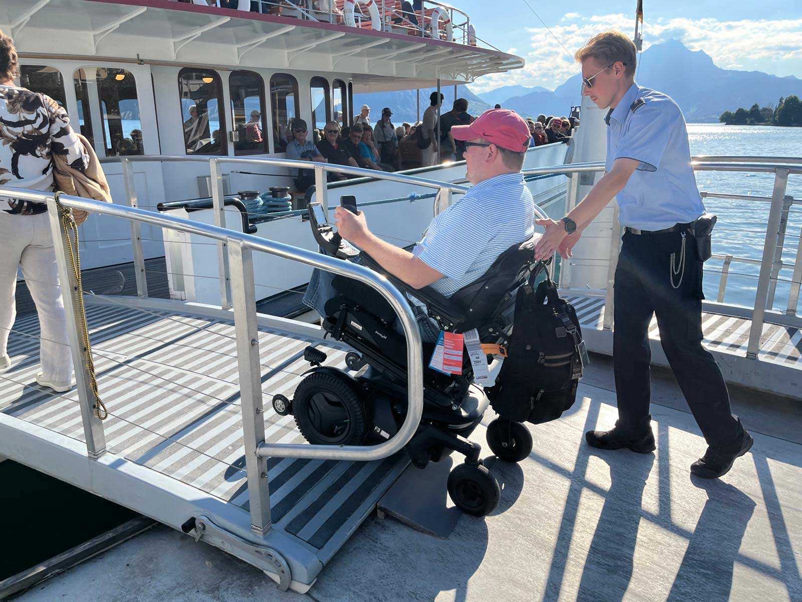 John driving his wheelchair across a ramp onto a ferry.
