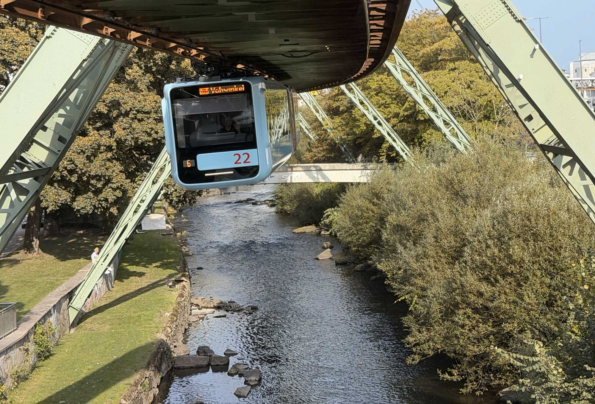 Schwebebahn train suspended from overhead track above a river.