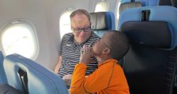 John and Robert talking while seated next to each other on an airplane.