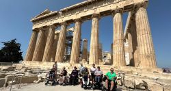 Group of wheelchair users in front of the Parthenon with its enormous marble pillars on the Acropolis hill in Athens, Greece.