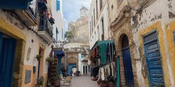 Moroccan street with shops, colorful doors and a fortified building in the distance with a tower above the city.