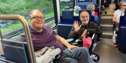 John pictured sitting on a train with a fellow wheelchair user.