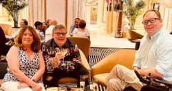 John seated with two friends, male and female, at a lounge area with multiple drinks on a table.