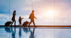 Three passengers of different sizes and ages walking through an airport terminal with luggage.