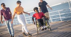 Young black wheelchair user with his friends on a boardwalk near the ocean.