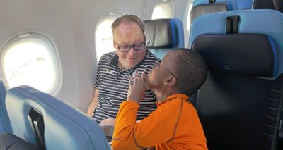 John and Robert talking while seated next to each other on an airplane.