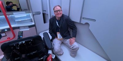 John seated on an adult-sized changing table in an airplane lavatory concept.