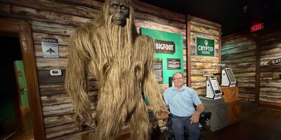 John seated in his wheelchair next to a larger-than-life Bigfoot statue.