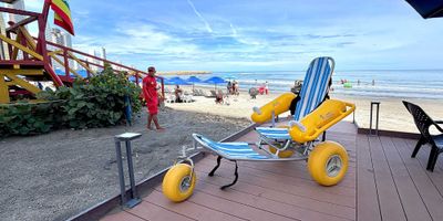 Beach wheelchair with large yellow tires on boardwalk in front of beach.