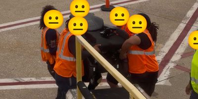 United Airlines baggage handlers manually carrying a power wheelchair.