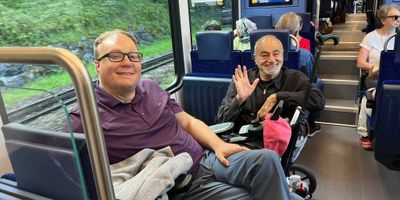 John pictured sitting on a train with a fellow wheelchair user.