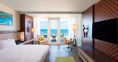 Hotel room with king size bed, wood floors and windows that look out over an oceanfront balcony.