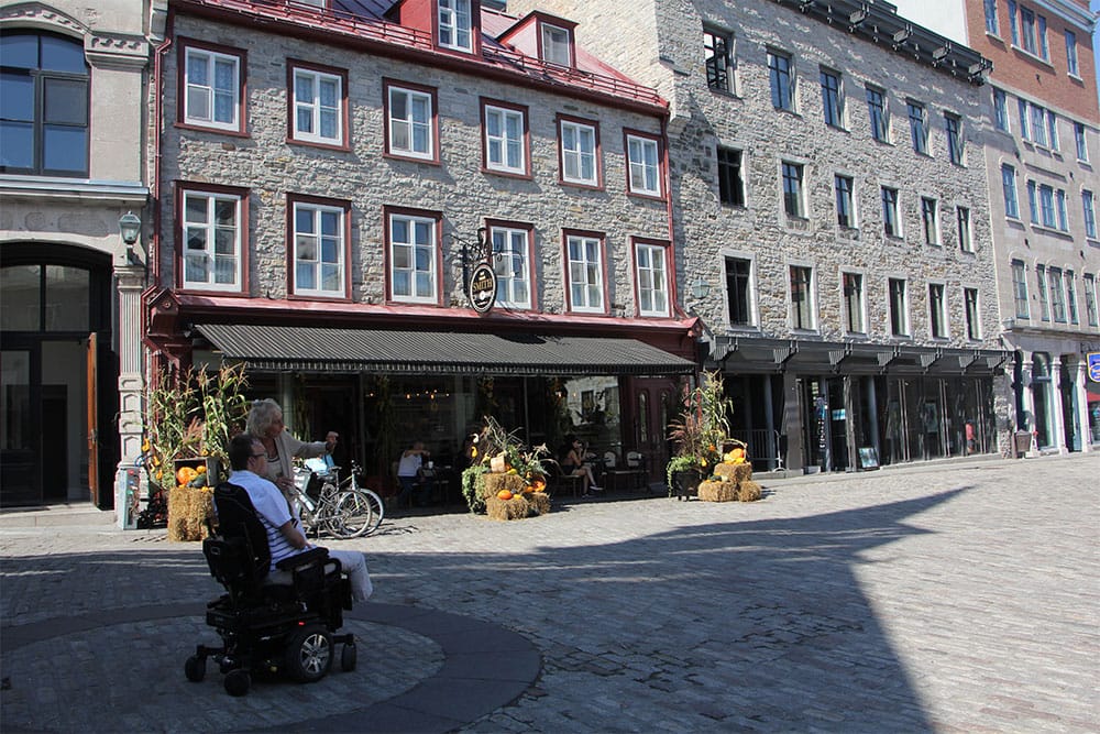 Wheelchair user in center of old town square with cobblestone pavement.