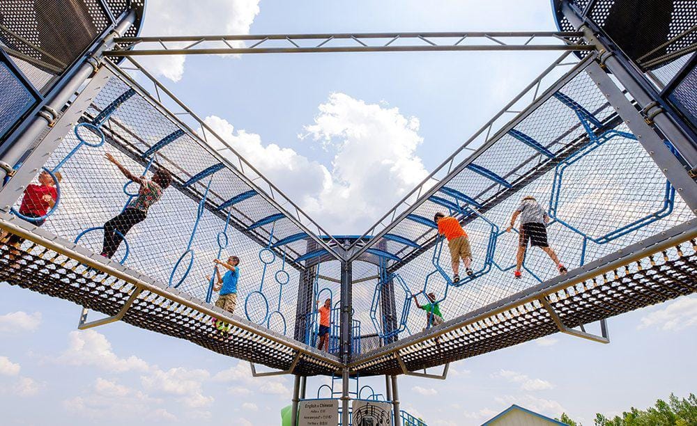 Children playing on climbing towers connected by sky bridges.