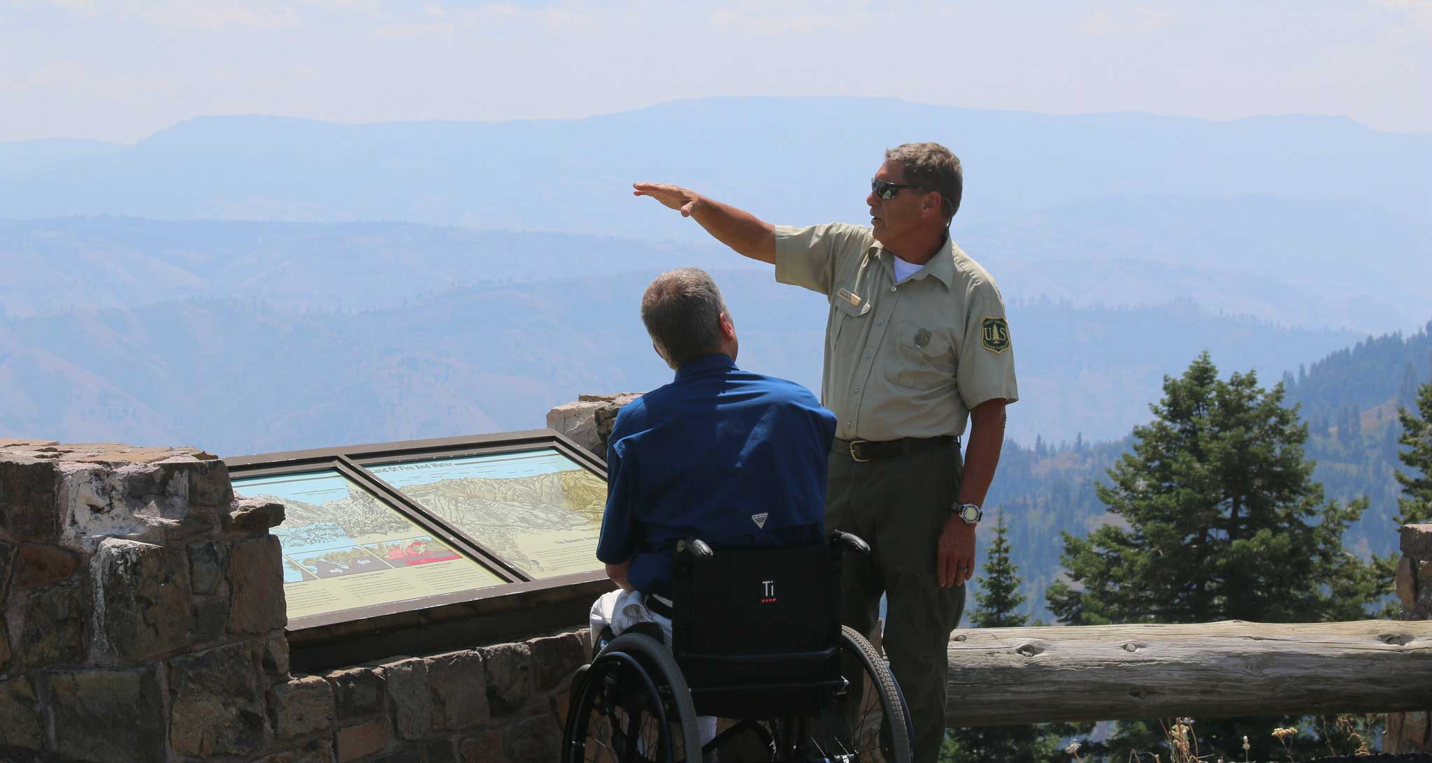 Park ranger speaking with a wheelchair user at an overlook inside a National Park.