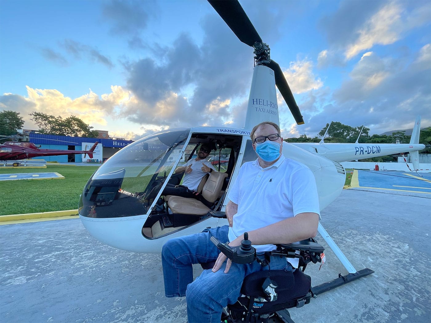 John seated in his wheelchair alongside a small, white helicopter.