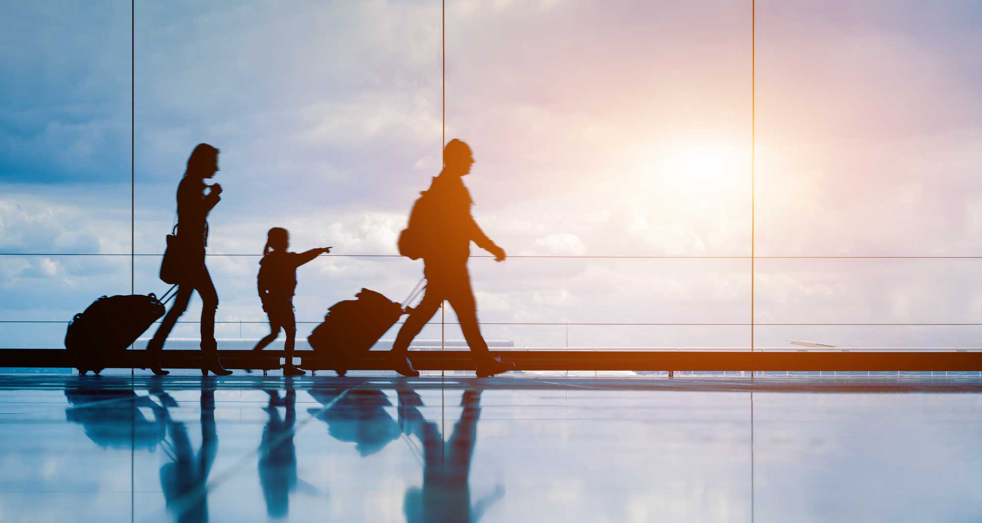 Three passengers of different sizes and ages walking through an airport terminal with luggage.