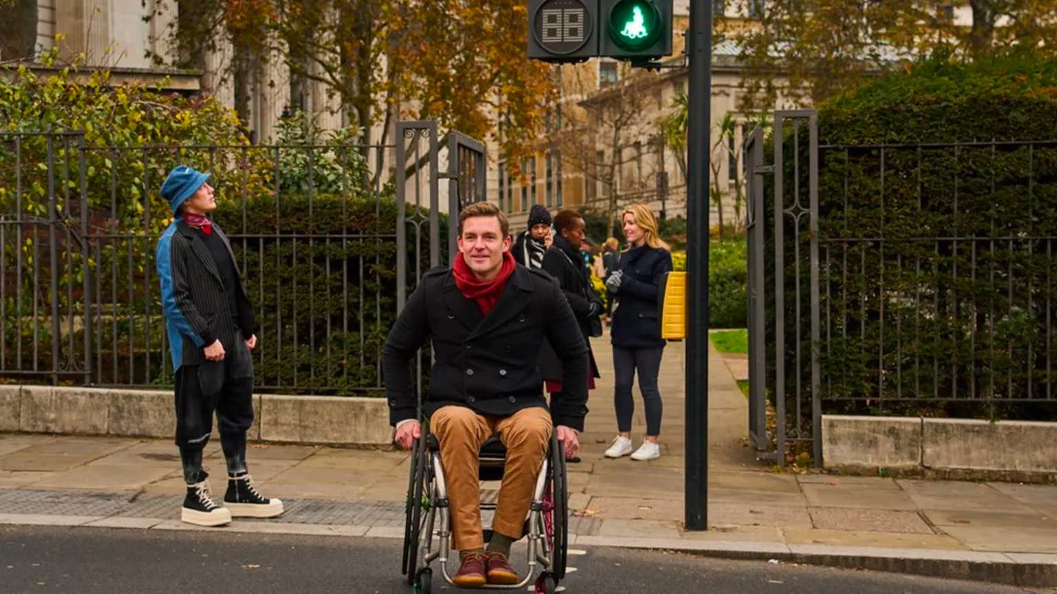 Male wheelchair user sitting beneath a crosswalk signal.