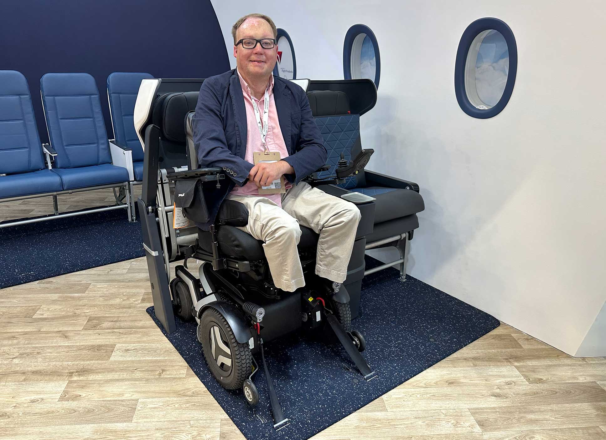 John seated in his wheelchair which is strapped to the floor of a model airplane.