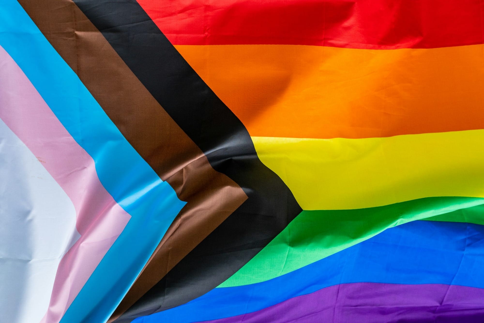A progress pride flag with colorful horizontal stripes and a chevron pattern