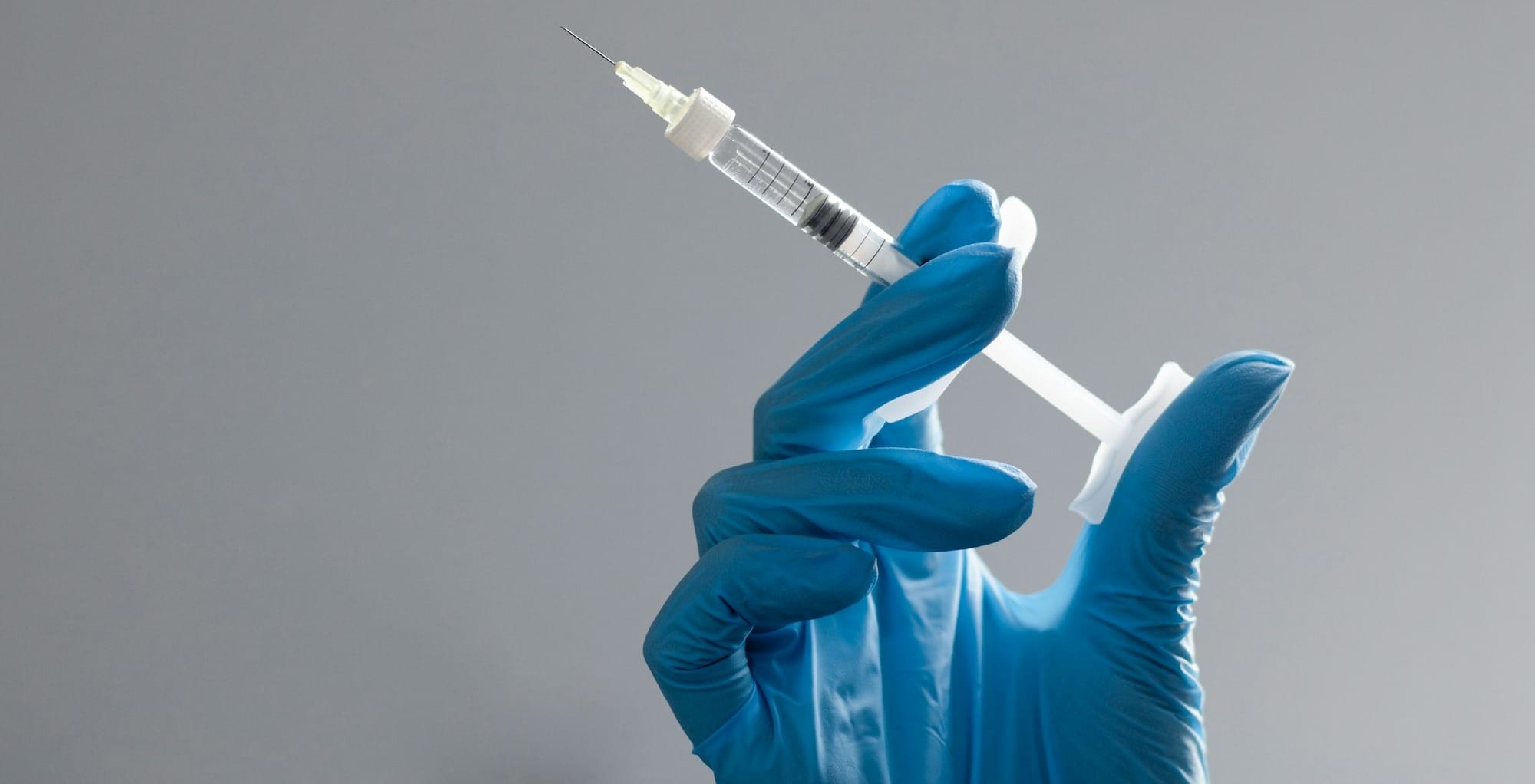 A hand in a glove holds a syringe