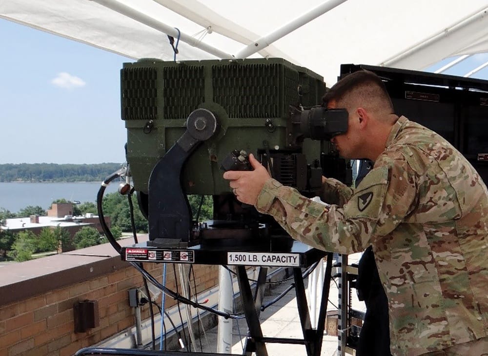 Soldier looking into the eyepiece of a large third-generation FLIR device mounted on a stand.