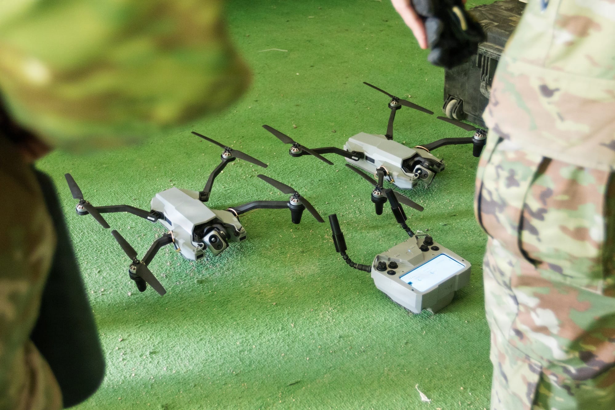 Two Black Widow quadcopters and a handheld controller rest on the ground beside soldiers at Fort Irwin.