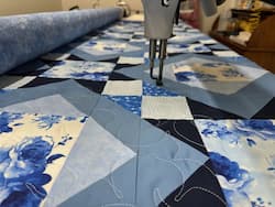A quilt on the longarm machine at Deb's Quilt Studio.  Beautiful blue and white rosy prints and coordinating shades of blue.  Depicts this quilting machine on a table