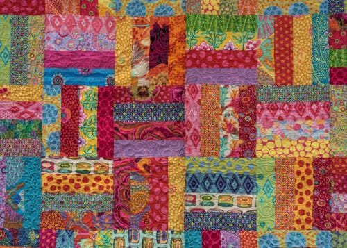 This strip quilt is made of a lot of different colored fabric strips with dots, prints, solids and geometric patterns. 