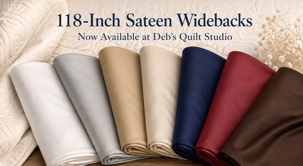 Seven folded 118-inch sateen wideback fabrics in white, light grey, tea stain, natural, navy, burgundy and brown at Deb’s Quilt Studio.