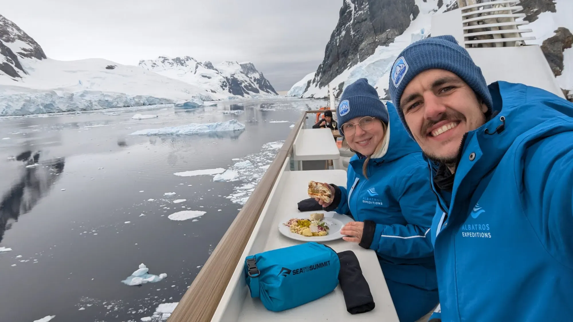 Katja und Nicolas beim Mittagessen an Deck des Expeditionsschiffs, im Hintergrund Gletscher und Eisschollen