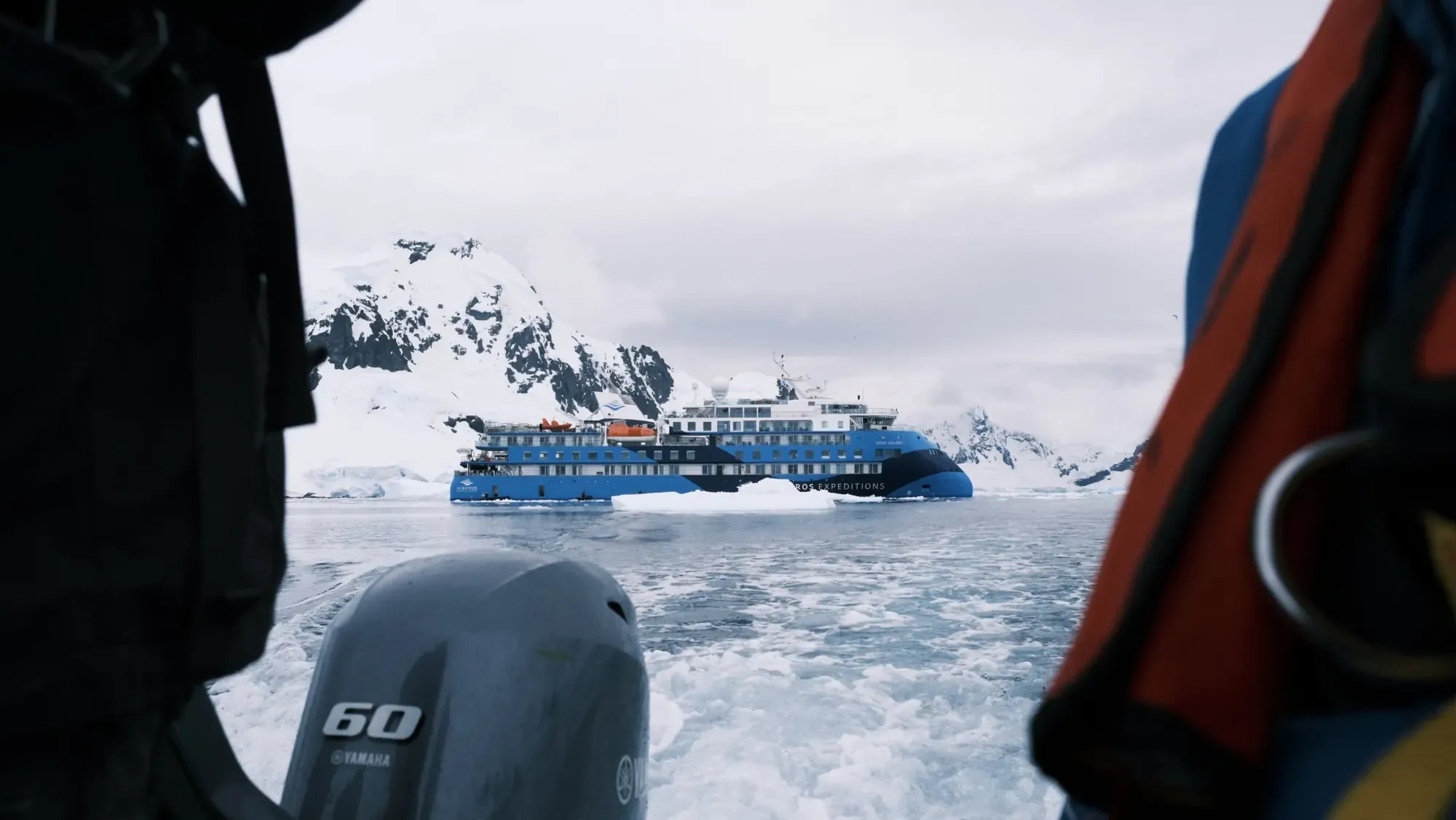 Blick aus dem Zodiac mit Aussenbordmotor auf das Expeditionsschiff Ocean Albatros zwischen Eisschollen und verschneiten Bergen