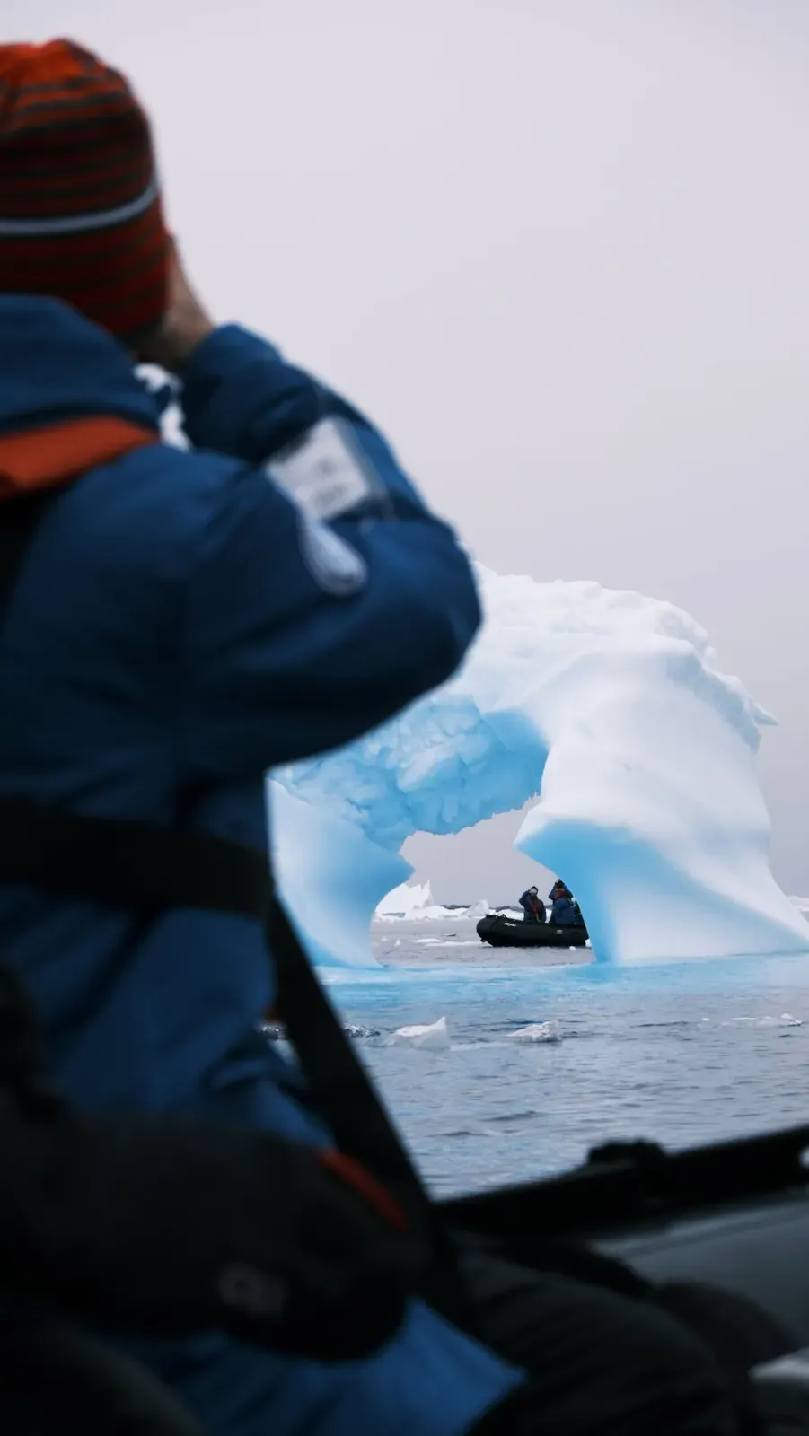 Ein Gast im Zodiac fotografiert einen Eisbogen, durch den Bogen ist ein zweites Zodiac mit Gästen in Expeditionsjacken zu sehen