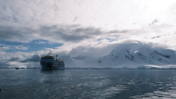 Das Expeditionsschiff Ocean Albatros vor verschneiten Bergen in der Antarktis, links ein Zodiac auf ruhigem Wasser