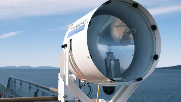 Suchscheinwerfer an Deck des Expeditionsschiffs, dahinter ruhiges Meer und Hügel am Horizont