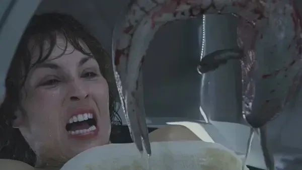 A screencap from the film Prometheus. The character played by Noomi Rapace makes a face of pure horror and disgust as a squid-like alien is held over her abdomen in a surgical pod.