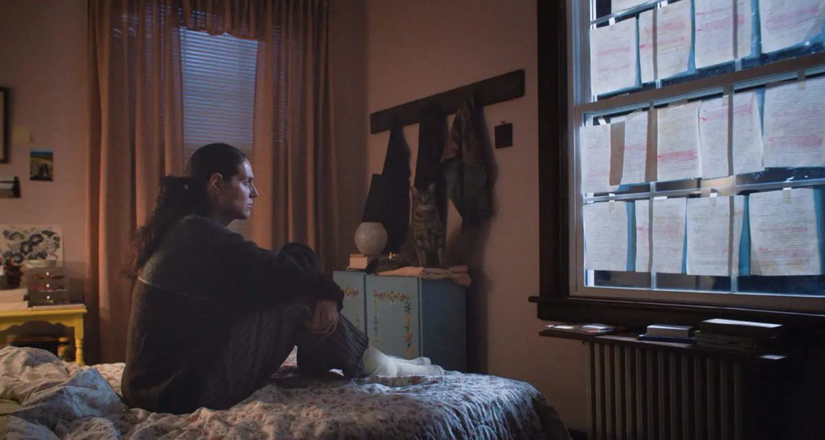 Eva Victor in a still from Sorry, Baby, looking at a window taped up with pages of a paper.