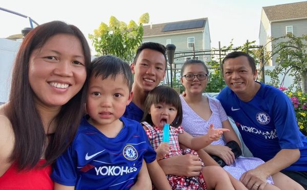 An Asian woman in her late thirties smiles on the left, and an Asian man smiles on the right. In between them are their four children, toddler to to teenage.