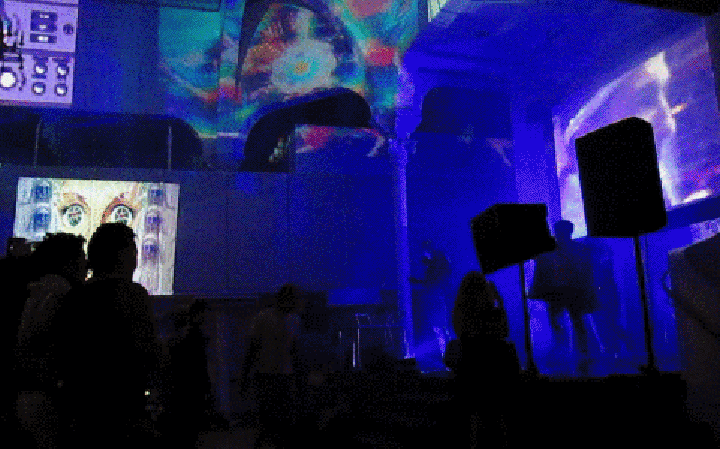 Flashes of light and a smoke machine surround the band Kids on TV amidst multi-channel GIF projections in a dark-lit community centre/theatre.