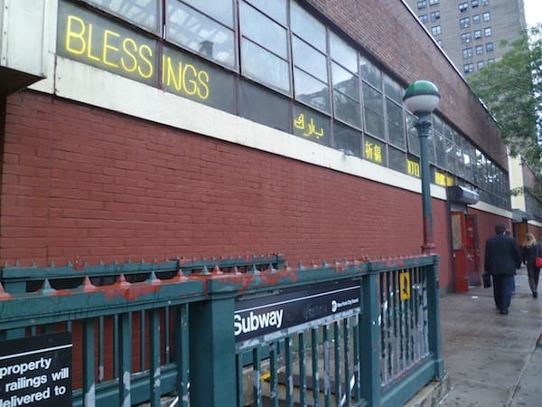 Carolina Caycedo's installation lit up in 5 different languages outside the historic Essex Street Market everytime someone came up from the subway exit pictured. (photo by Janelle Grace for Hyperallergic)