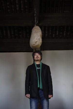 Artist Wu Yuren beneath a hanging stone.