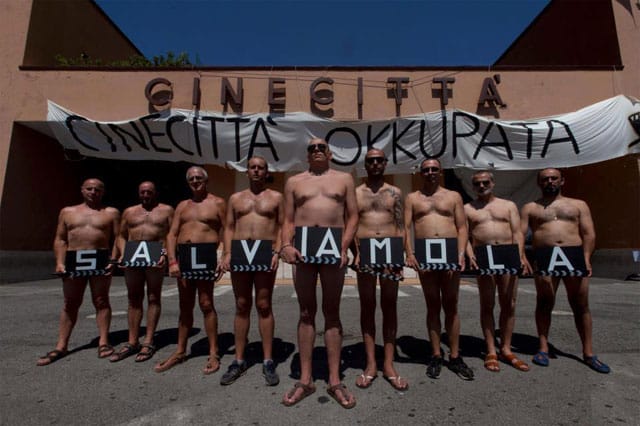 Some of the occupying Cinecitta workers hold up signs saying, "Let's save her [Cinecitta]." 