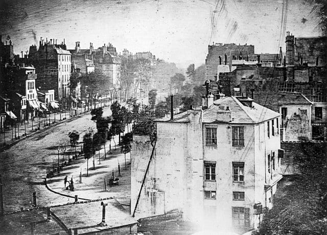 view of the Boulevard du Temple in Paris by Louis Daguerre from 1838, believed to be the first photograph of a person (via Wikimedia)