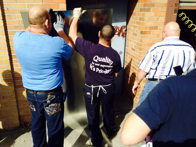 Workers from the company that owns the door covering up the new Greenpoint Banksy with a metal sheet. (photo by the author for Hyperallergic)