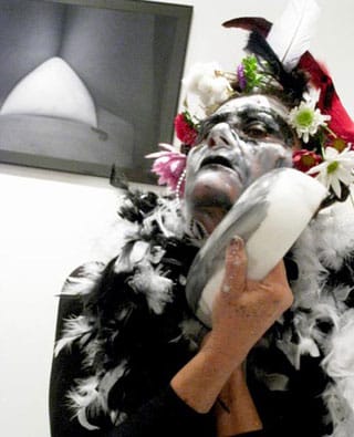Angela Freiberger mixing face paint with her sculpture “PwE (Plate with Eye)” (2010);  her photograph “Vulva Place” (2010) hangs overhead. (click to enlarge)