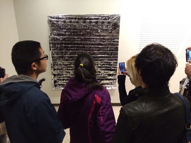 Guggenheim museum visitors reading and photographing G.U.L.F.'s manifesto, which they posted in the museum during their intervention. (photo by the author for Hyperallergic)