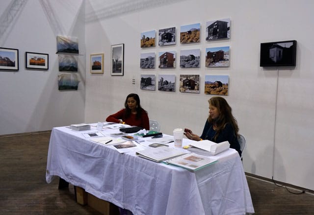 Marcia Cooper's booth, with the 'Resistance Shelter' photos arranged in a grid and the 'Lost Site, Cite, Sight' pieces on the left side of the back corner