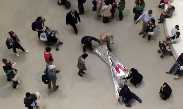 A Guggenheim security official in a beige suit stopping protesters from unfurling a banner in the atrium of the Upper East Side Museum. (screenshot from a video shot by the author for Hyperallergic)